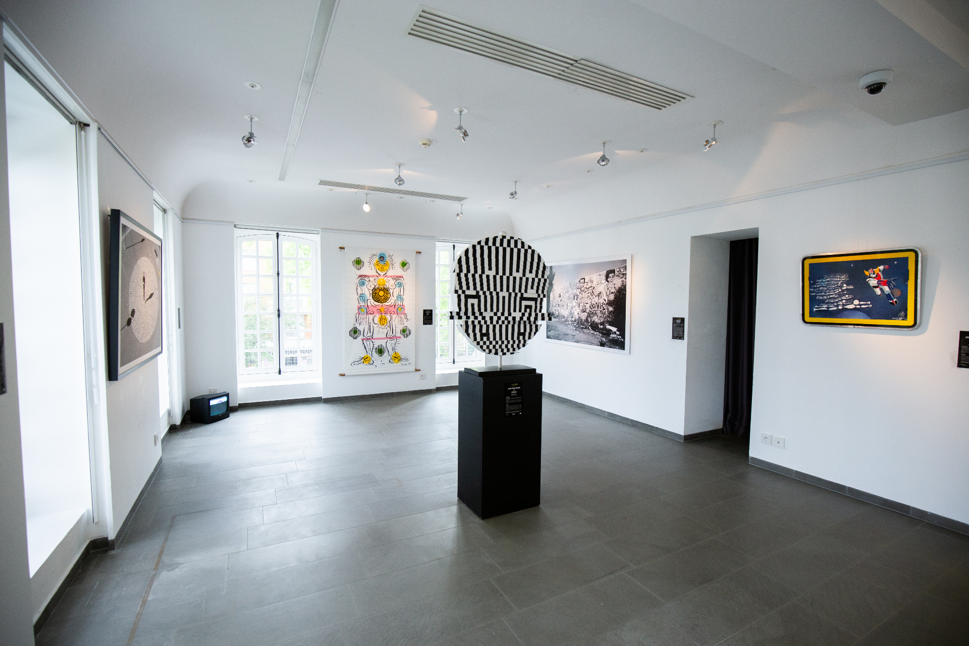 Salle d'exposition avec sculpture centrale et œuvres aux murs